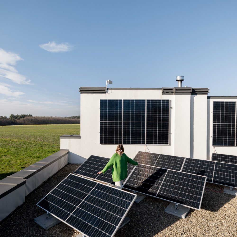 Wide view from above on a solar power plant installed on rooftop of household on nature, happy owner walks on it. Alternative energy, independence and sustainable lifestyle concept